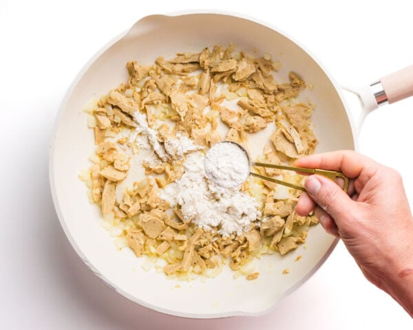 Flour is being sprinkled over a skillet with other ingredients.