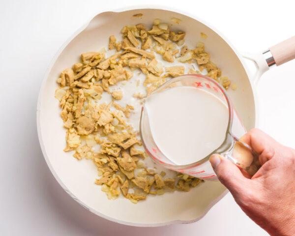 Oat milk is being poured into a skillet with other ingredients.