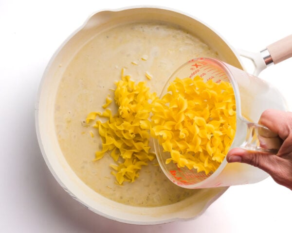 Pasta is being poured into a skillet with a milky mixutre.