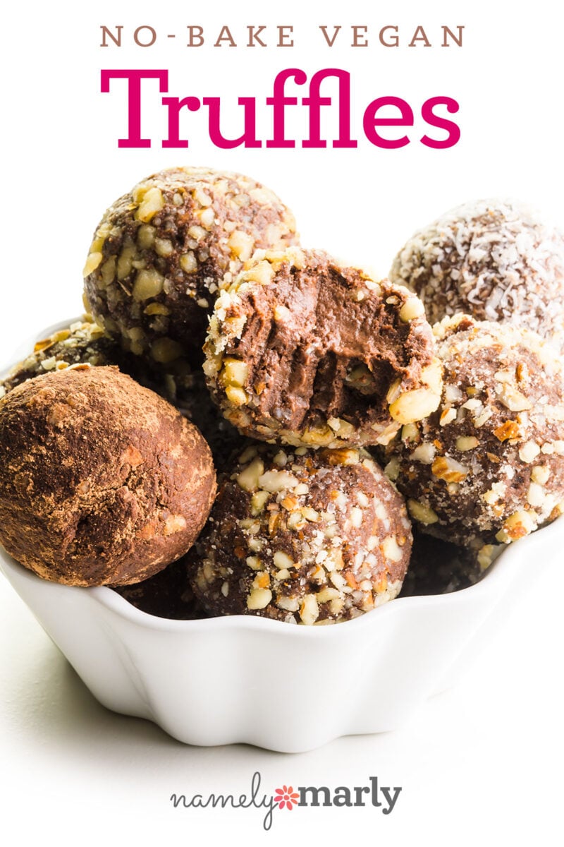 No-bake vegan truffles in a white bowl, coated with nuts and cocoa powder, some with a bite taken out.