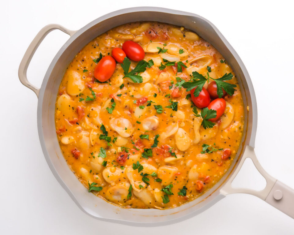 A saucepan is filled with a creamy sauce with beans, tomatoes, and fresh herbs on top.