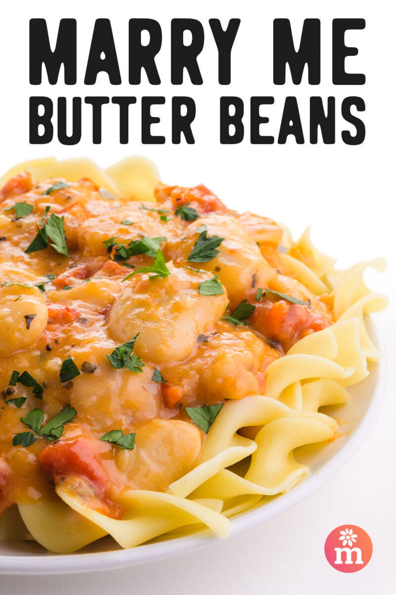 Creamy butter beans in tomato sauce served over wide noodles, topped with fresh parsley.