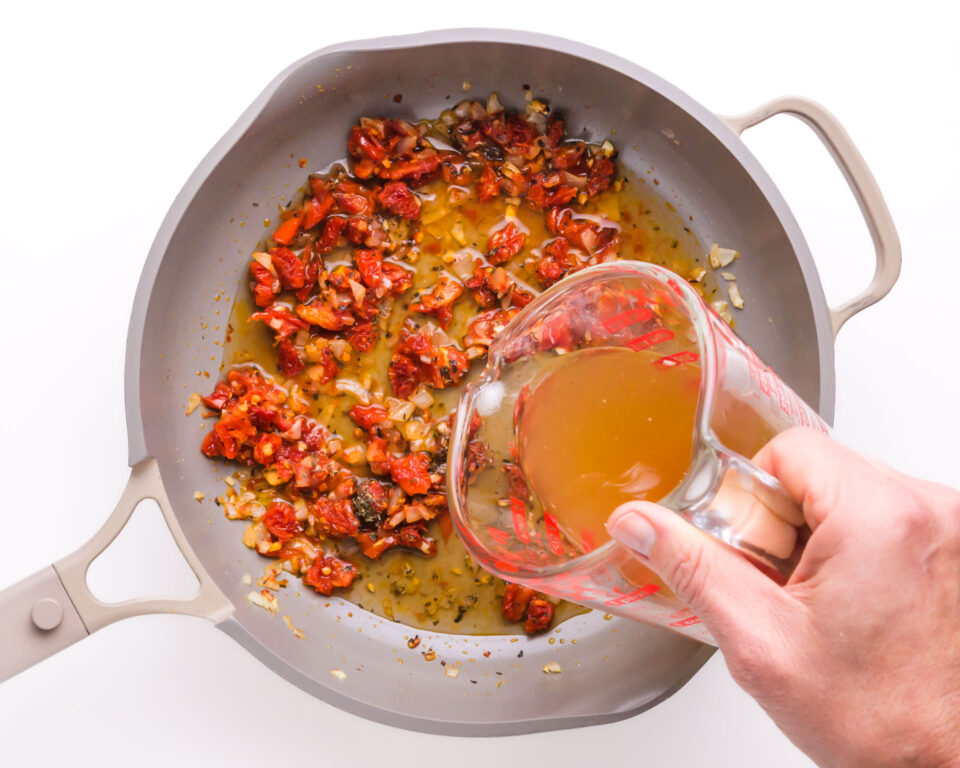 Vegetable broth is being poured into a skillet with other ingredients.