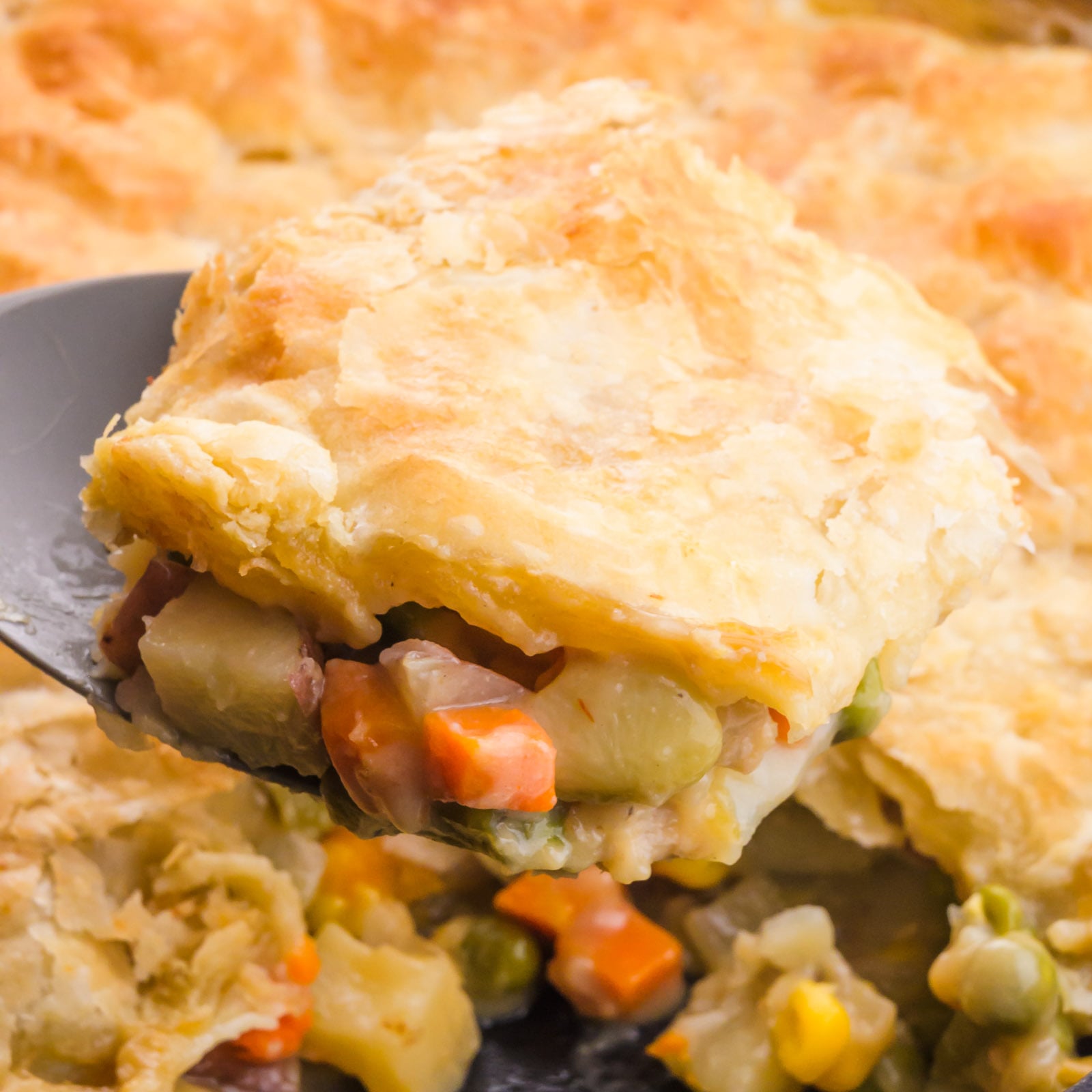 A serving of vegan chicken pot pie hovers over the skillet it was made in.