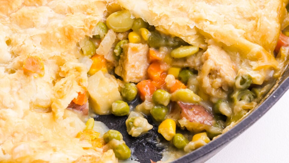 Looking into a skillet with pot pie and a bite taken out revealing the vegetables and sauce inside.