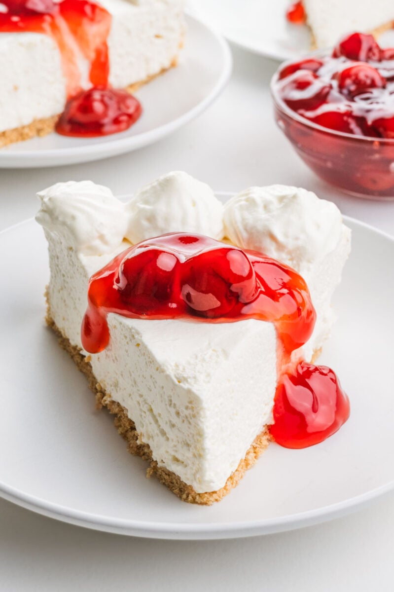A slice of no-bake cheesecake on a plate has cherry sauce on top.