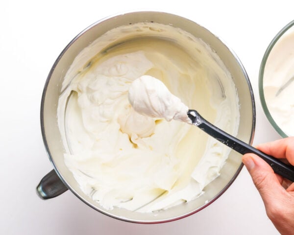 A cream cheese mixture is being spooned into a mixing bowl with whipped cream.