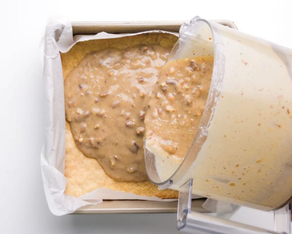 Pecan filling is being poured into a pan with a baked crust.