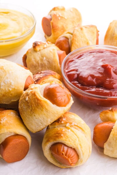 Vegan pigs in a blanket are situated around bowls of ketchup and mustard.