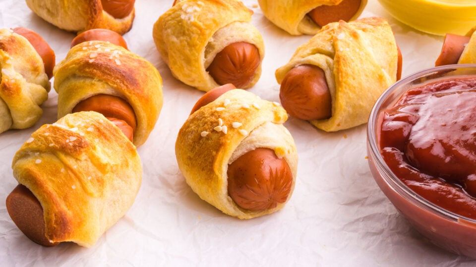 Vegan pigs in a blanket sit next to a bowl of ketchup.
