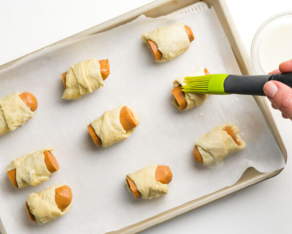 Vegan pigs in a blanket are being brushed with oat milk for browning.