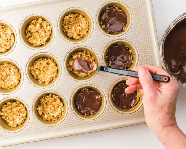 Chocolate sauce is being drizzled over oat mixture in muffin pan compartments.