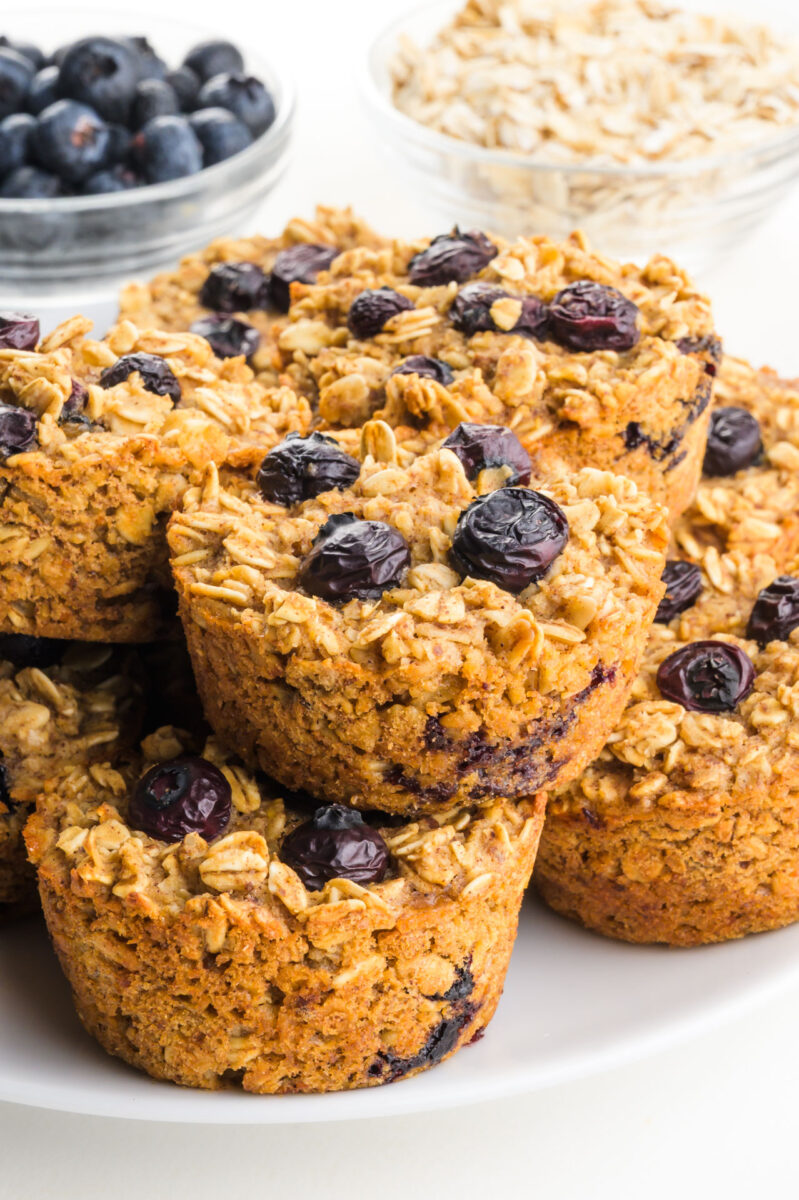 Blueberry Oat Cups stacked on a plate with fresh blueberries and oats in the background.