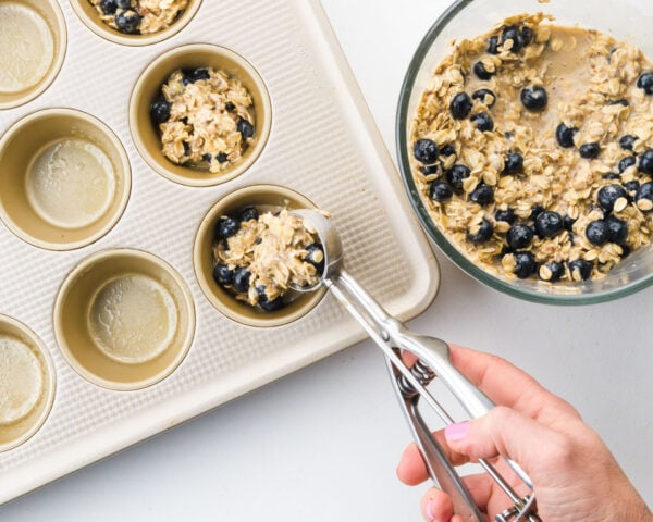 Blueberry oatmeal batter is being distributed into a muffin pan.