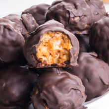 A bunch of crunchy peanut butter balls on a plate shows one with a bite taken out.