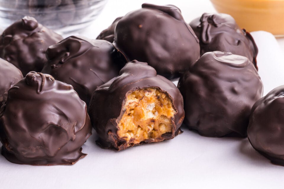 Chocolate Covered Crispy Peanut Butter Balls on a table, one with a bite taken out.