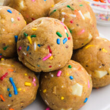 Colorful, ball-shaped cookie dough bites topped with sprinkles, stacked on each other.