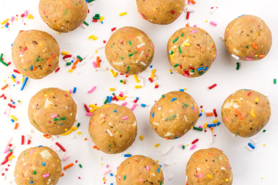 Cookie dough balls topped with colorful sprinkles on a white background.