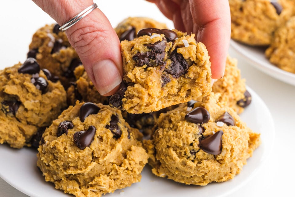 A hand holds a chewy chickpea choc chip cookie showcasing lots of melted chocolate chips.