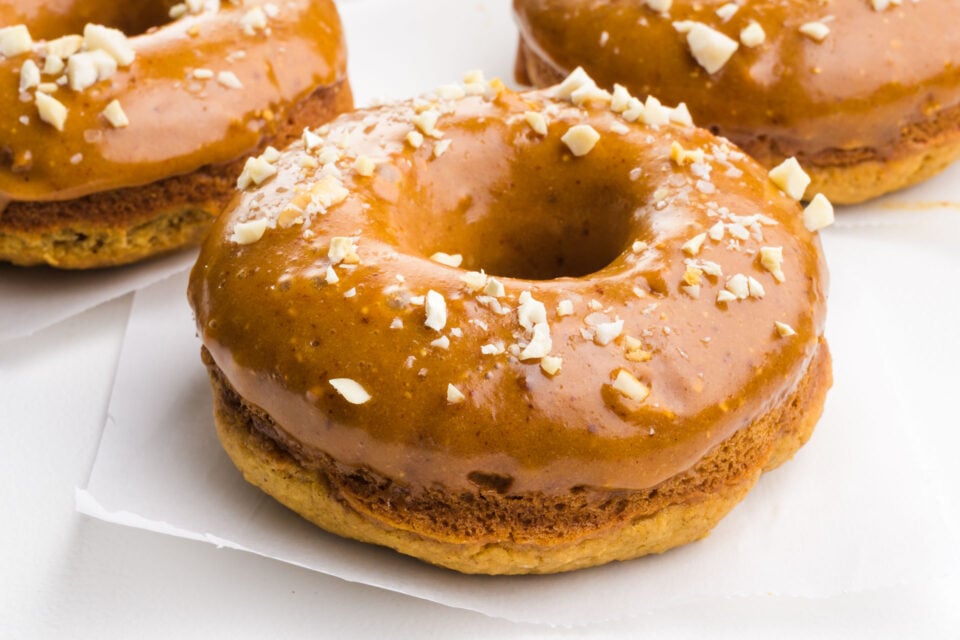 A closeup of three peanut butter donuts, all with glaze and chopped nuts on top.