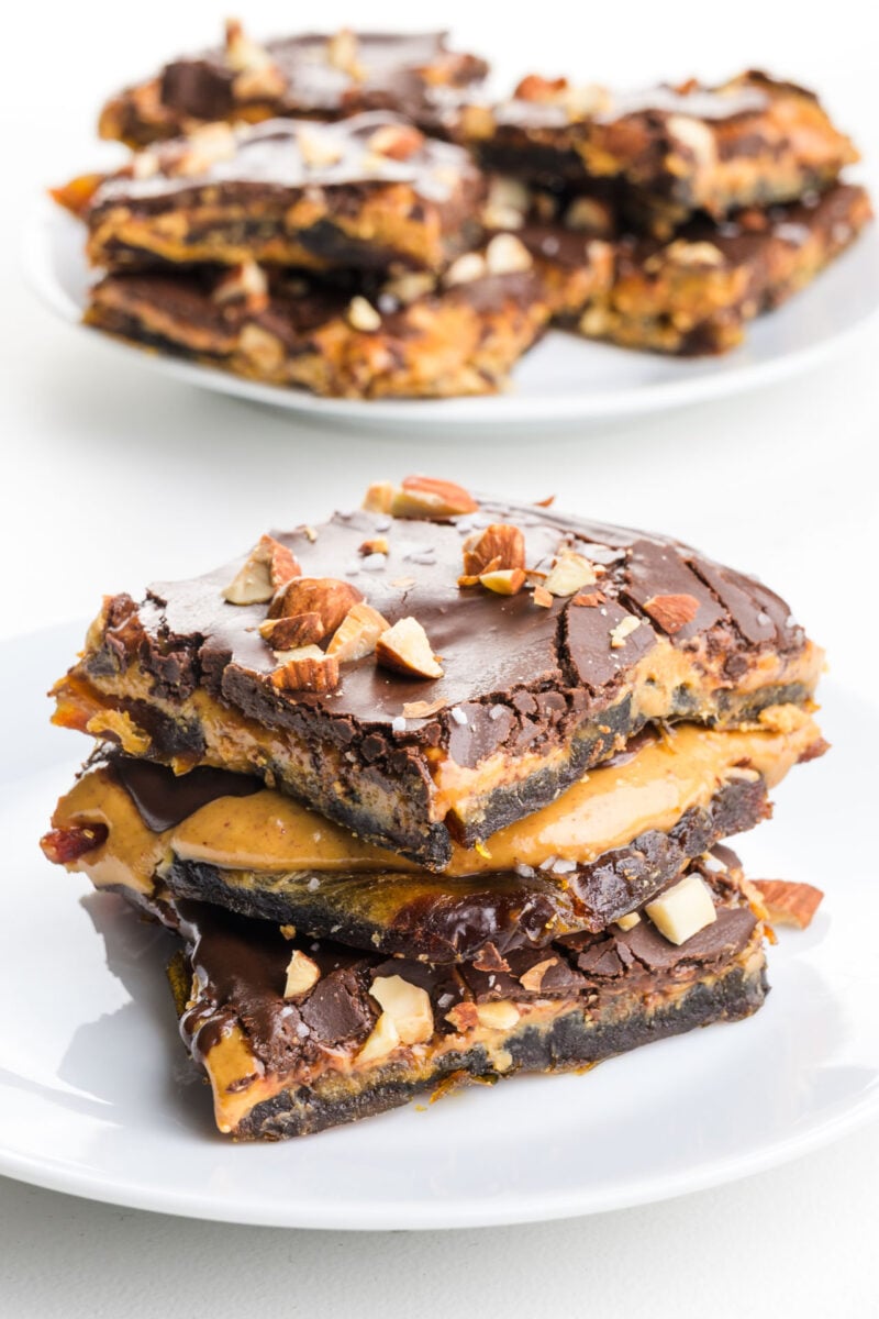 Three slices of viral date bark on a plate feature gooey peanut butter and dark chocolate with chopped almonds on top.