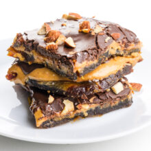 A stack of date bark slices are on a white plate with chopped almonds on top.