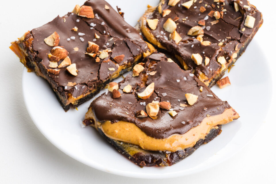 Three slices of date bark showcase a rich peanut butter layer with crispy chocolate on top and chopped nuts.