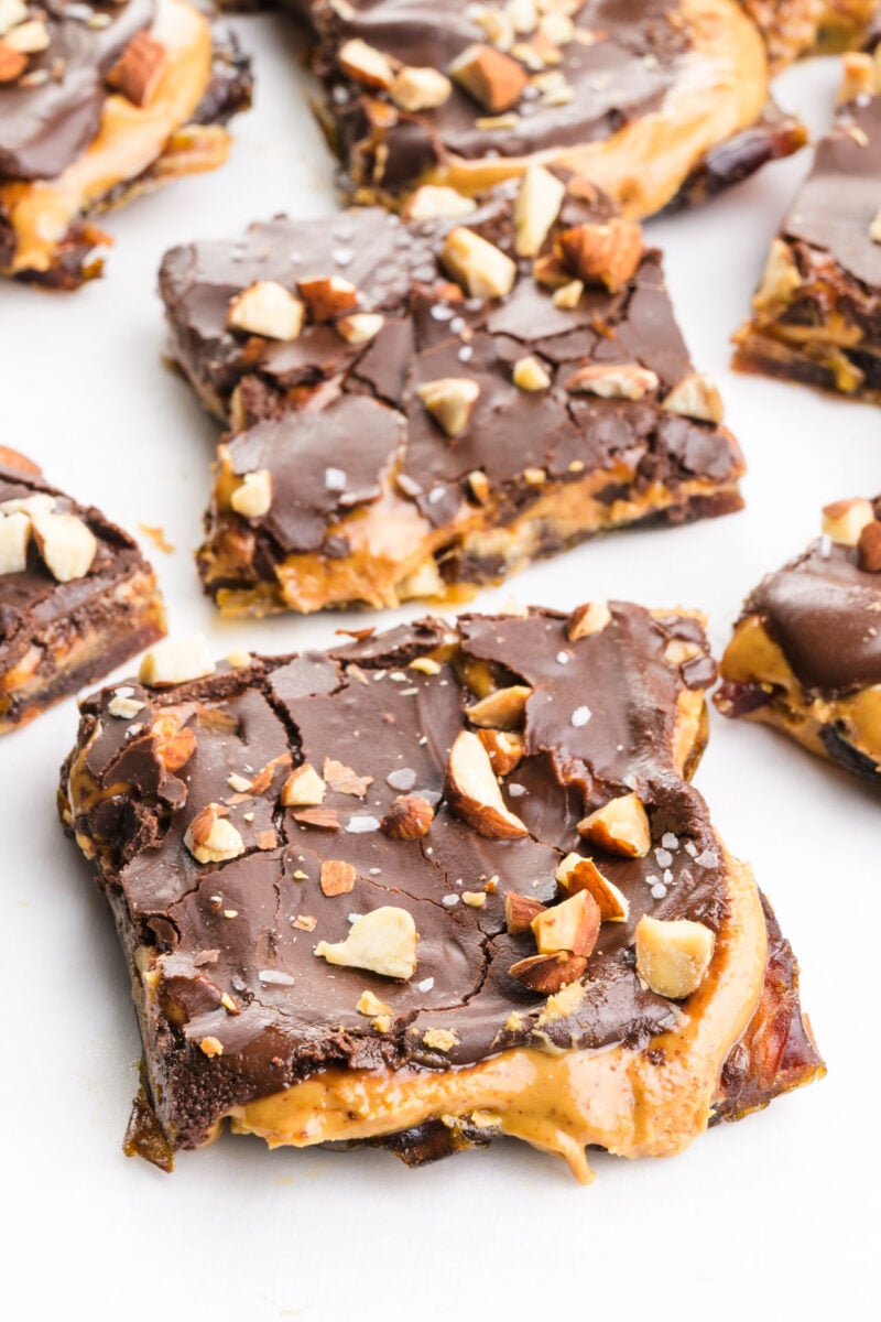 Several slices of dark chocolate date bark feature a gooey peanut butter layer and chopped almonds on top.