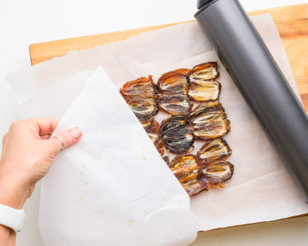 A rolling pin is used to flatten a layer of medjool dates between sheets of parchment paper.