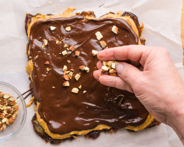 Roasted almonds are being added to snickers date bark while the chocolate is still wet.