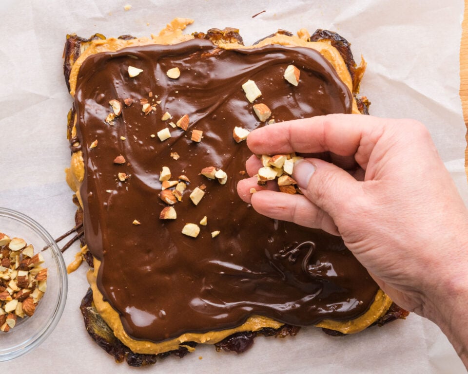 Roasted almonds are being added to snickers date bark while the chocolate is still wet.