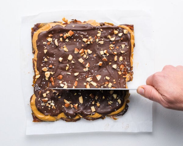 Chocolate peanut butter date bark is being cut with a knife into slices.