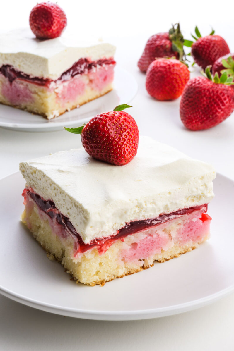 Vegan strawberry cake slice topped with a fresh strawberry, served on a white plate.