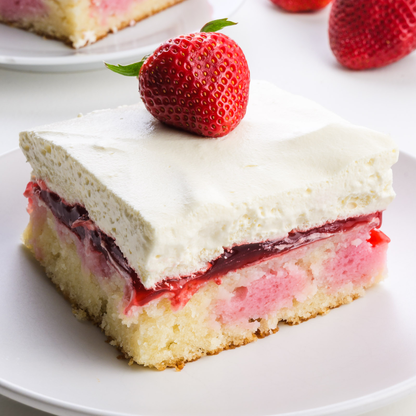 Vegan strawberry shortcake cake slice topped with a fresh strawberry, served on a white plate.