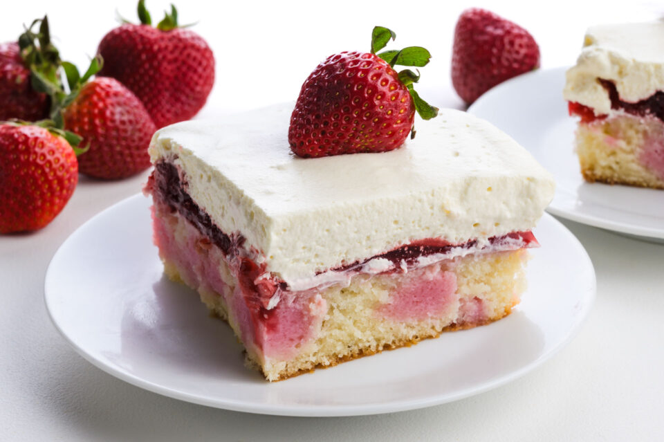 Vegan strawberry cake slice topped with a fresh strawberry, served on a white plate.