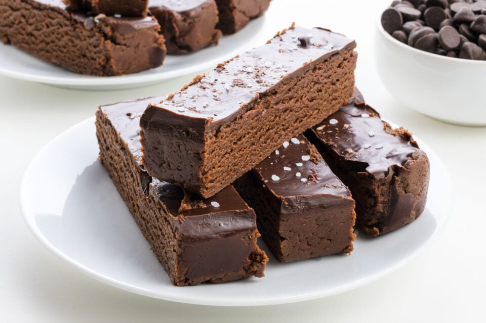 Chocolate protein bars with a glossy chocolate coating, sprinkled with sea salt on a white plate.