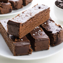 Chocolate Brownie Protein Bars topped with glossy chocolate and a sprinkle of sea salt, served on a white plate.