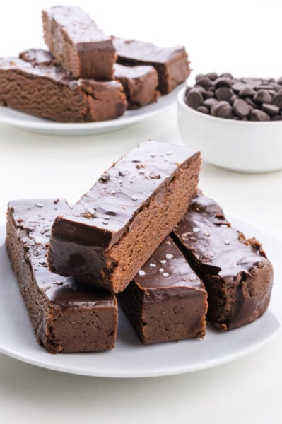 Chocolate Brownie Protein Bars with a glossy coating and a sprinkle of sea salt, accompanied by a bowl of chocolate chips.