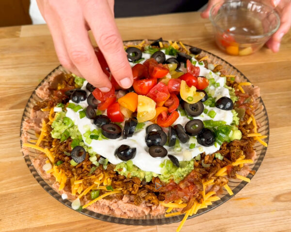 Layered dip with refried beans, cheese, guacamole, sour cream, diced tomatoes, olives, and green onions.