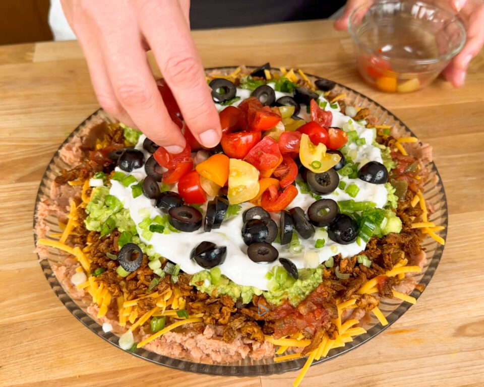 Layered dip with refried beans, cheese, guacamole, sour cream, diced tomatoes, olives, and green onions.