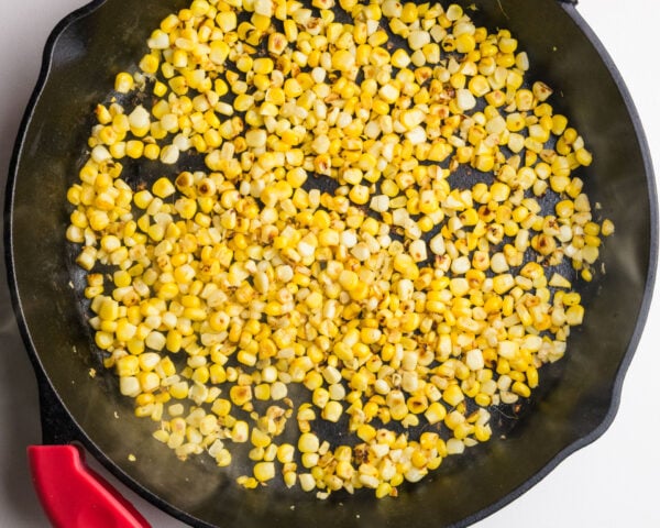 Pan of sautéed yellow corn kernels with some golden-brown spots in a cast-iron skillet.