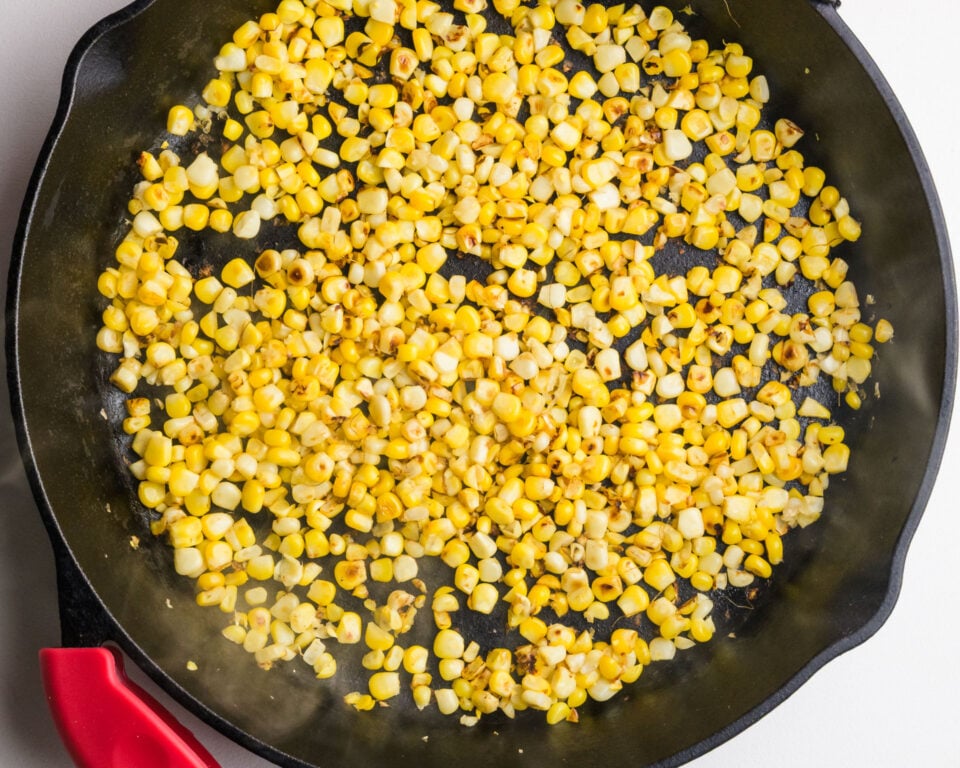 Pan of sautéed yellow corn kernels with some golden-brown spots in a cast-iron skillet.